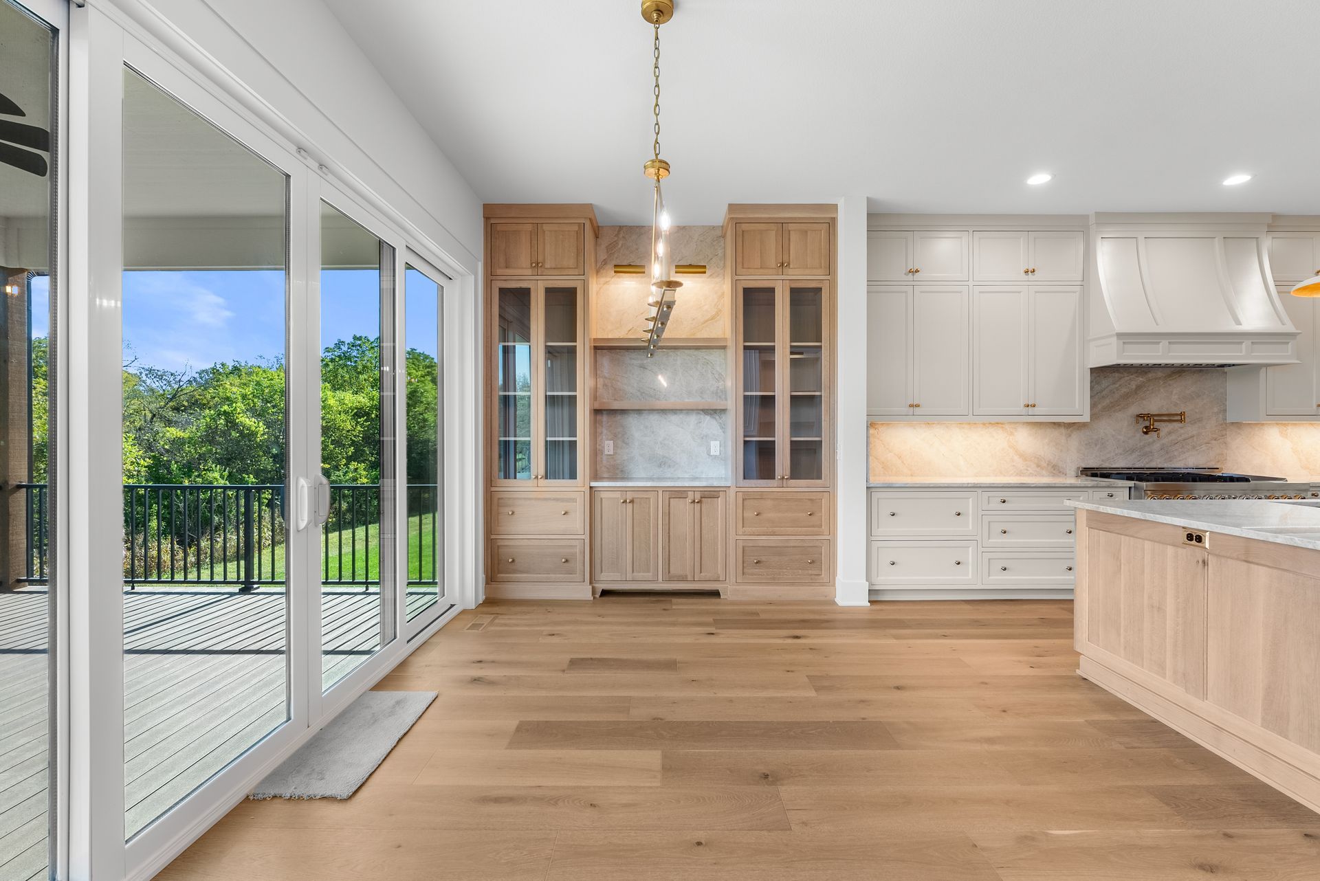 Spacious kitchen with wood cabinets, light wood floor, and large glass sliding doors overlooking a patio and green trees.