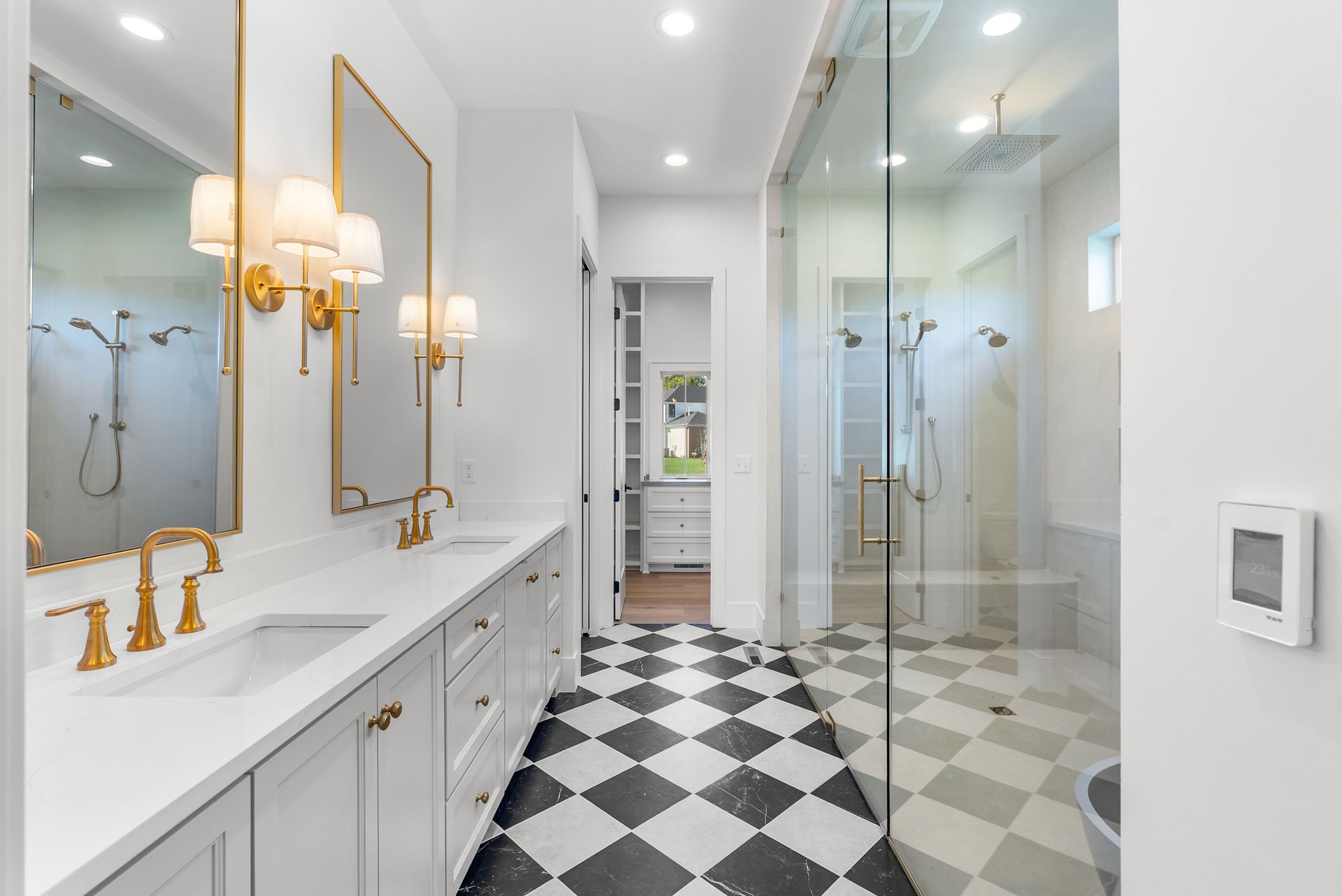 Spacious bathroom with black and white checkered floor, double sinks, gold fixtures, and glass shower.