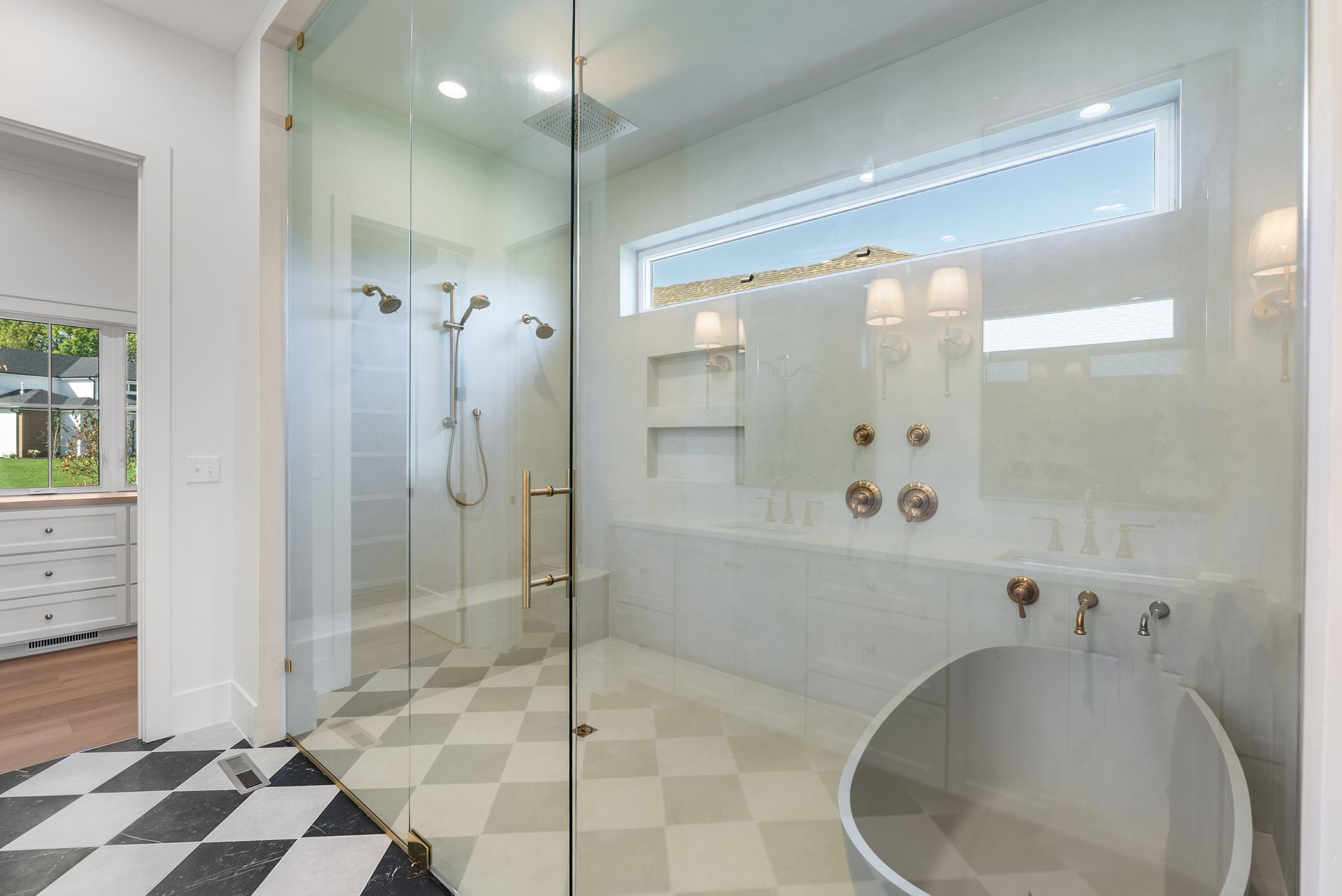 Spacious modern bathroom with shower, soaking tub, and checkered floor. White and gold accents, natural light.
