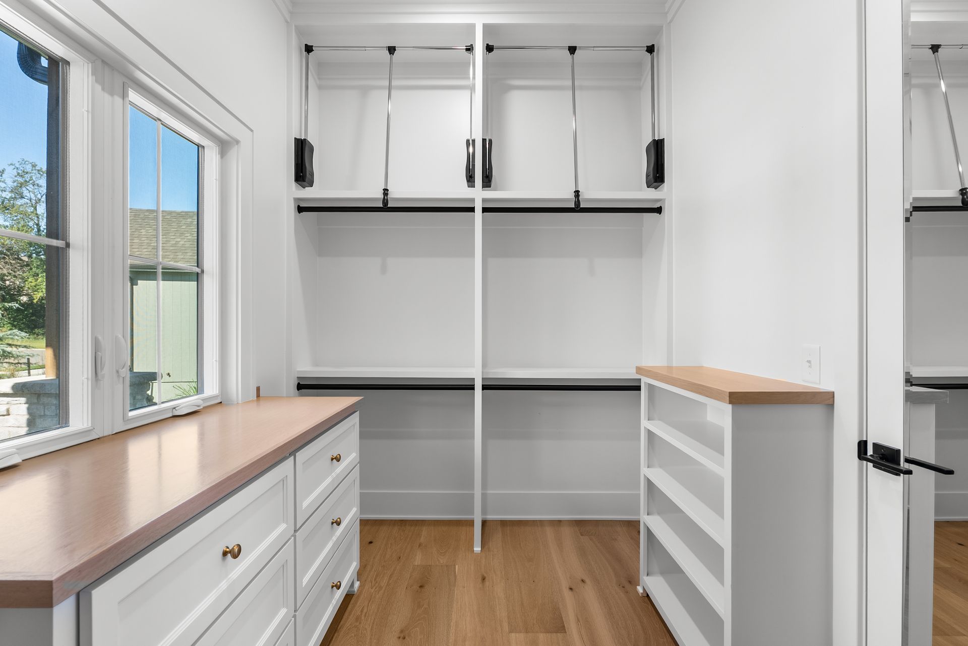 Empty walk-in closet with white walls, wood floors, and a dresser.
