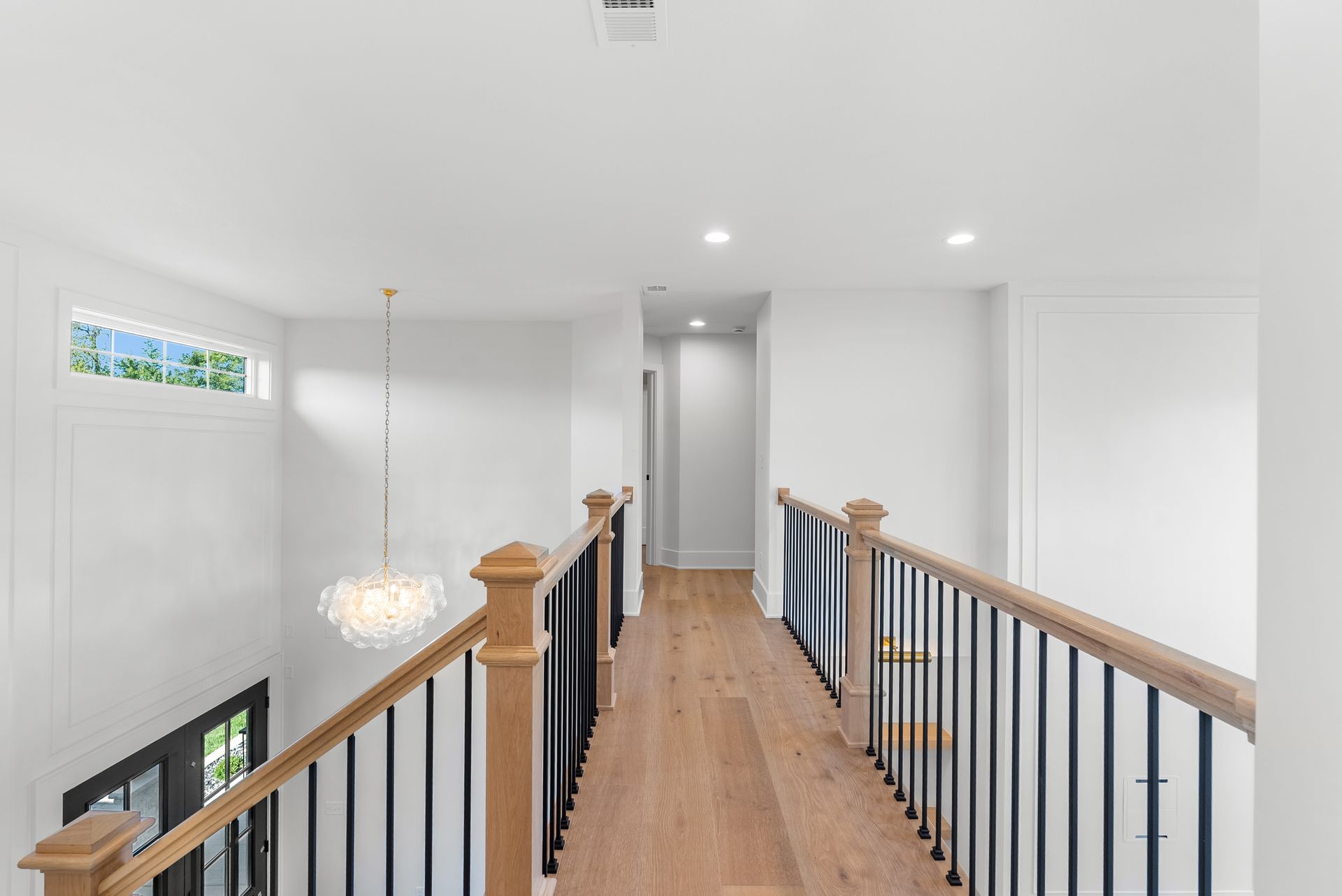 A bright, modern hallway with a wooden floor, black railing, and white walls.
