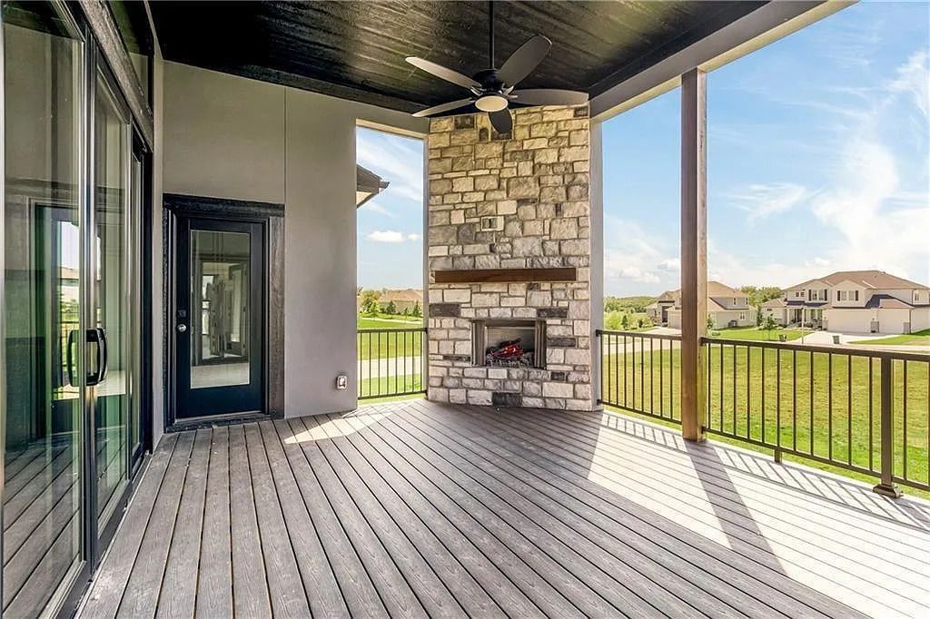 Covered outdoor patio with stone fireplace, wood deck, and glass doors.