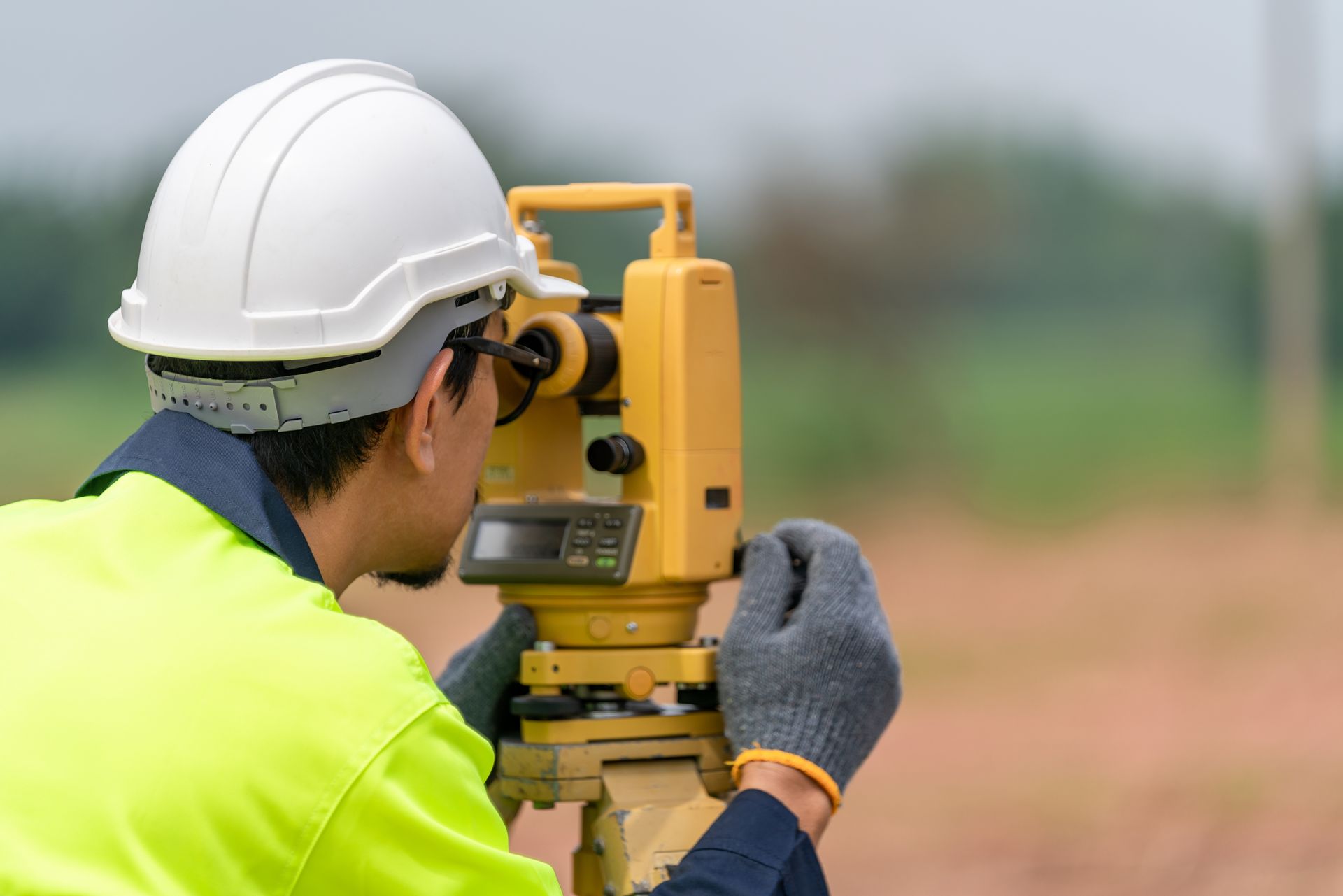 Surveyor in a hard hat and safety vest using a theodolite outdoors.