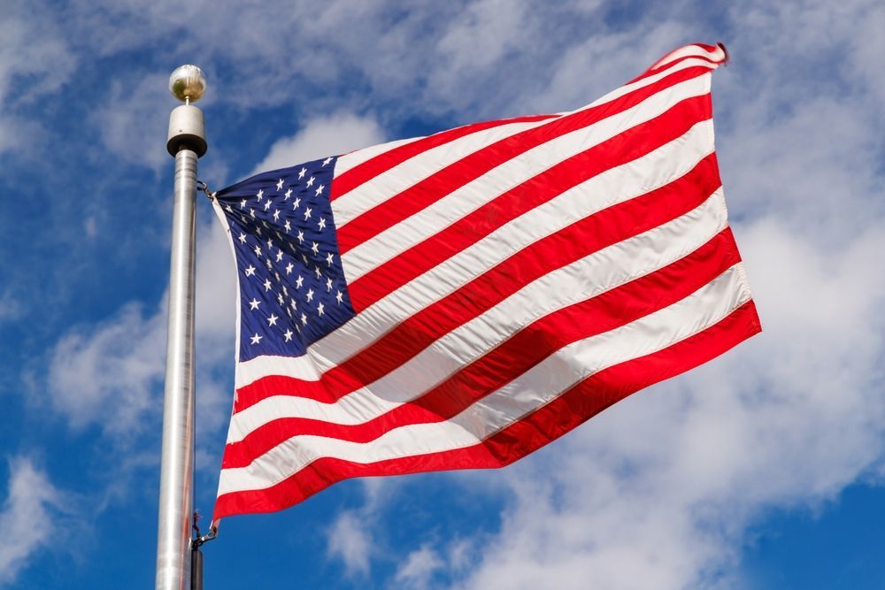American flag waving in the wind against a blue, cloudy sky.