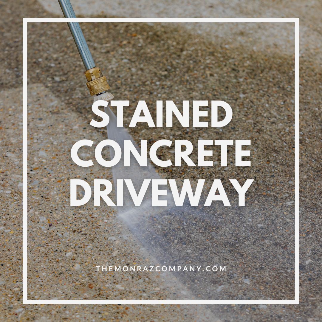 A person is using a pressure washer to clean a stained concrete driveway.