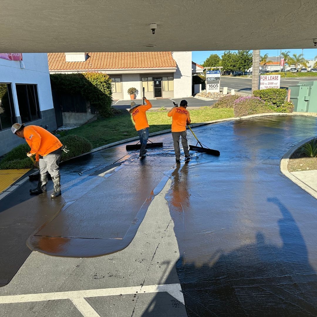 Three men in orange shirts are cleaning a parking lot.