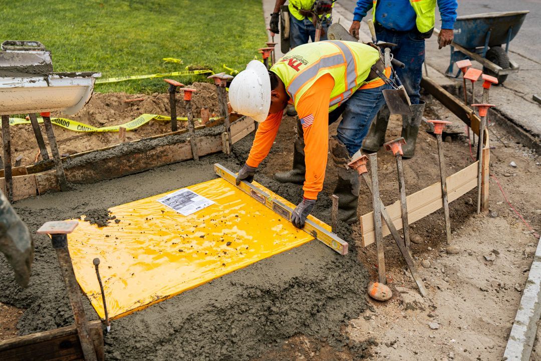 A group of construction workers are working on a sidewalk.