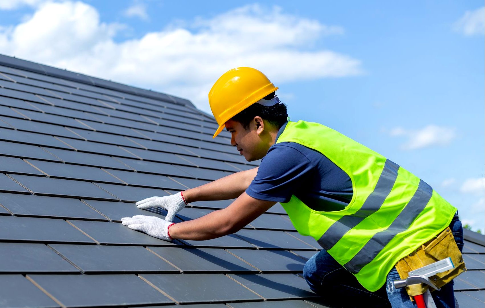 a man wearing a hard hat and safety vest is working on a roof .