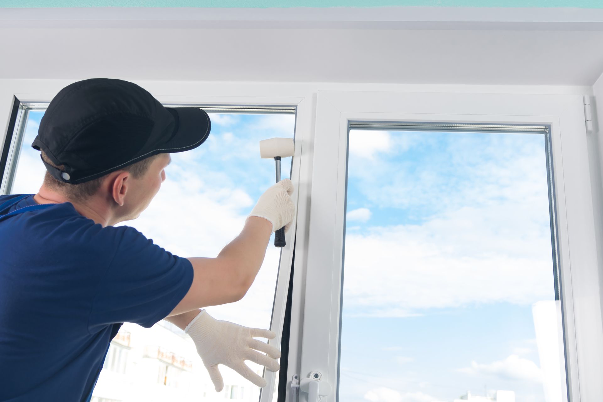 A builder installs a double-glazed window, hammering it with a rubber mallet. A builder installs a double-glazed window, hammering it with a rubber mallet.
