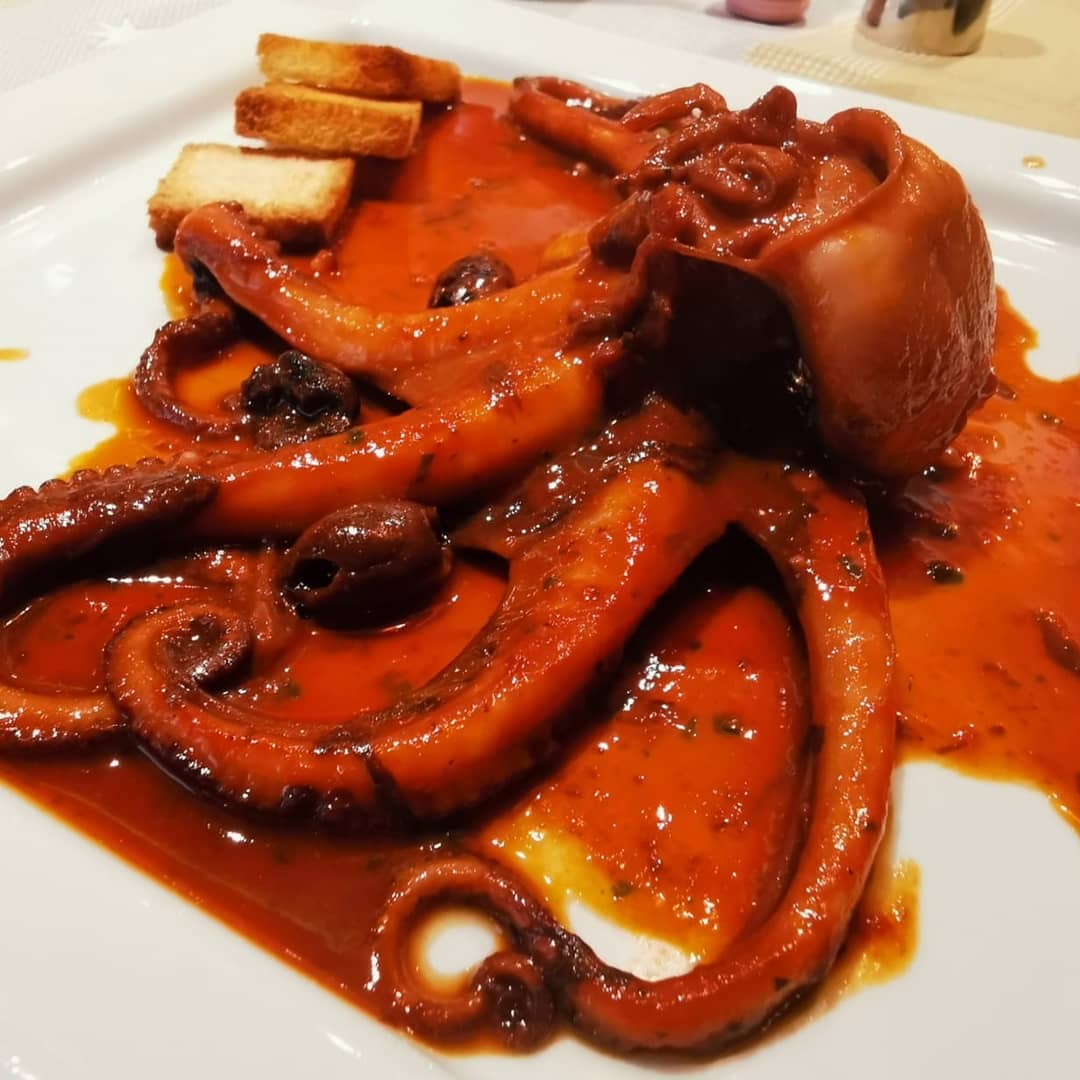 Un piatto bianco con sopra un polpo e salsa
