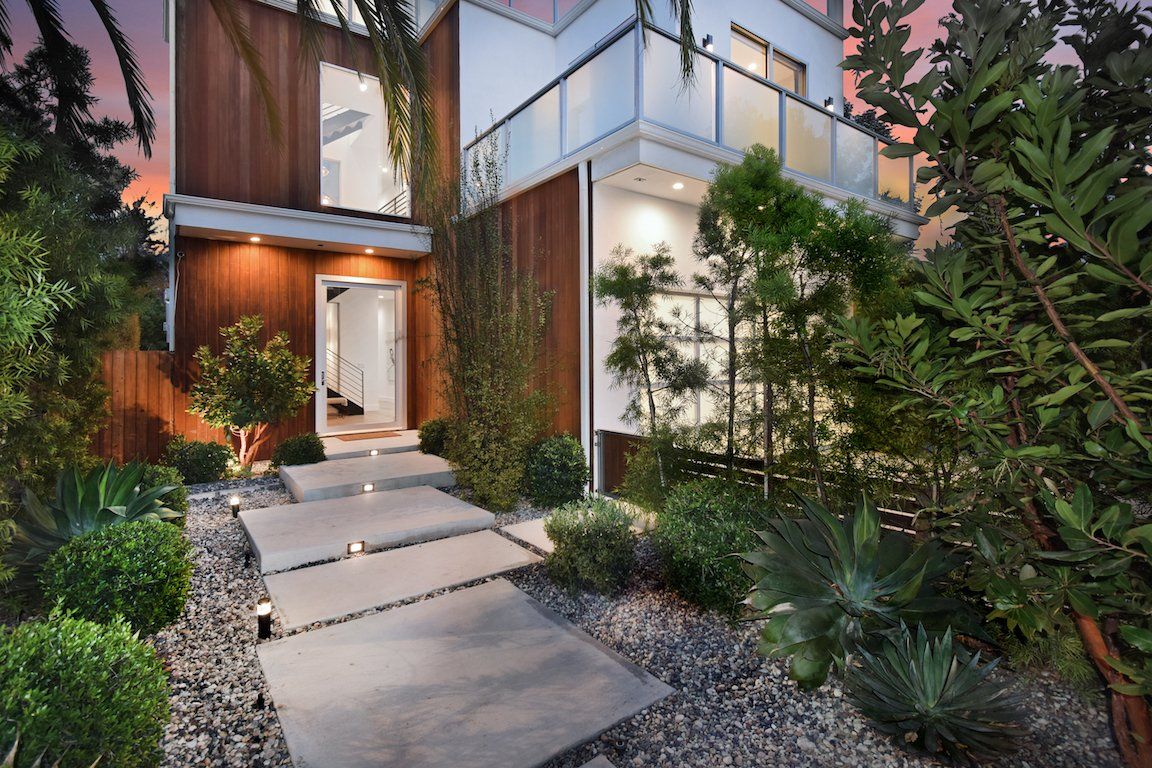 A modern house with a concrete walkway leading to the front door surrounded by trees and bushes.