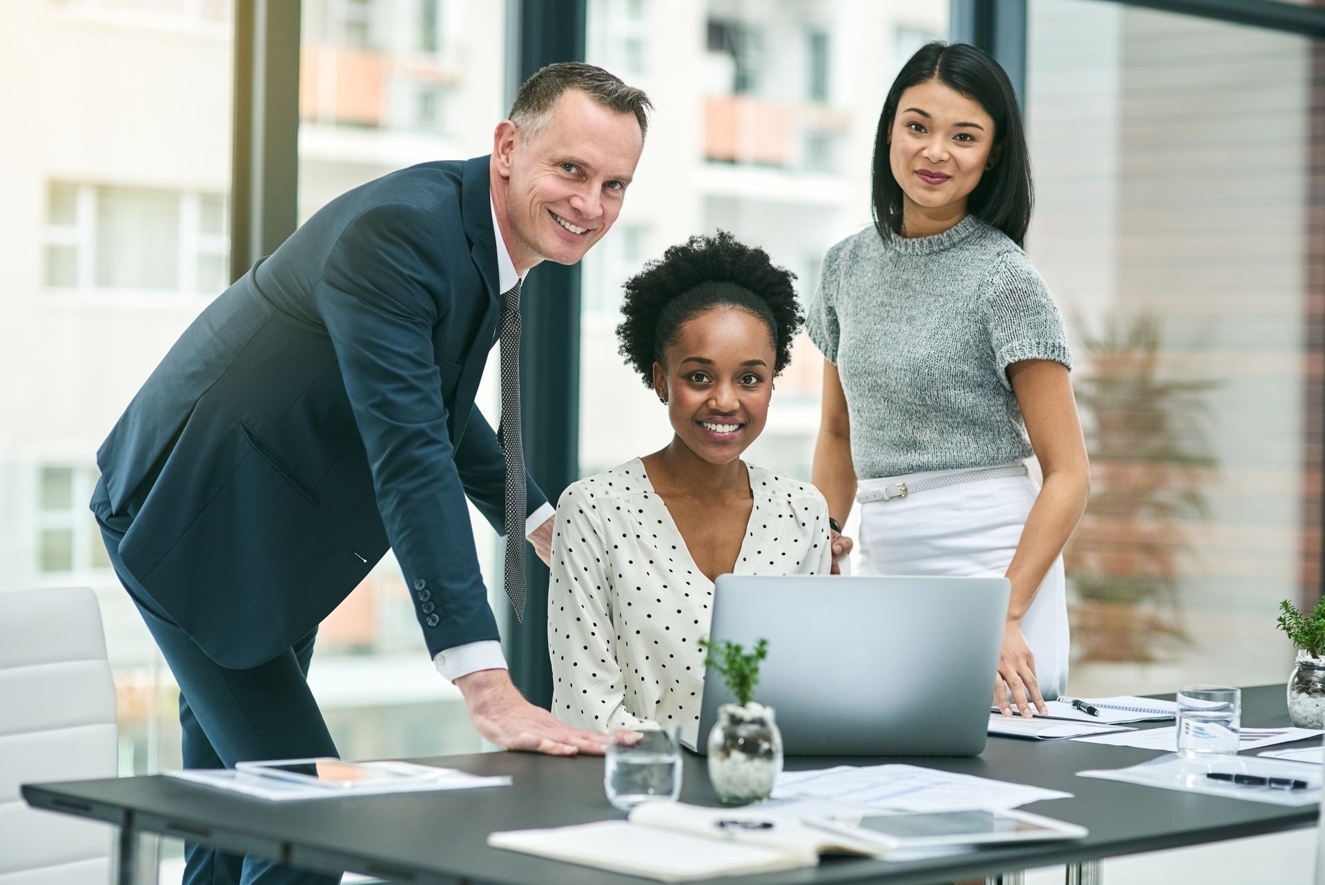 A group of people are standing around a table with a laptop computer.