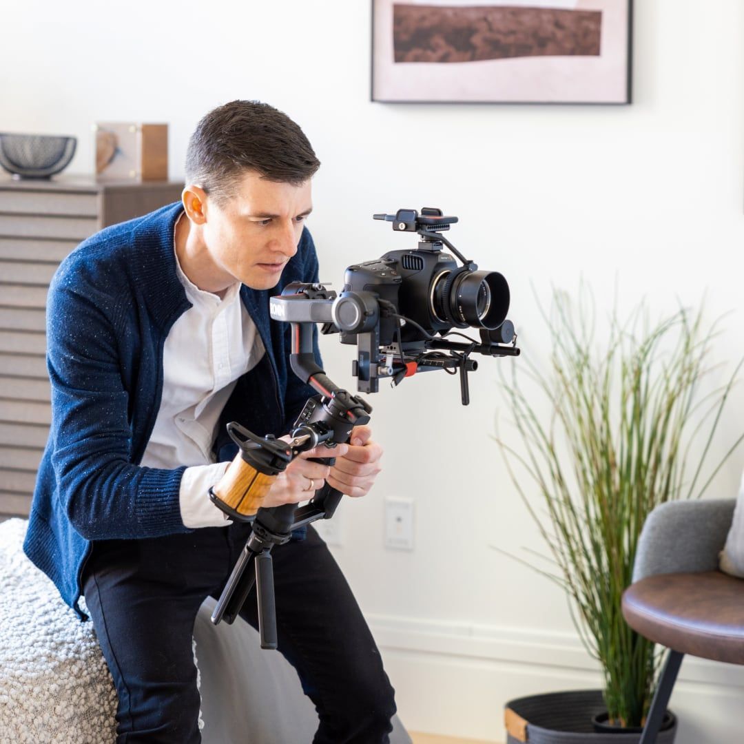 A man is sitting on a couch holding a camera on a tripod