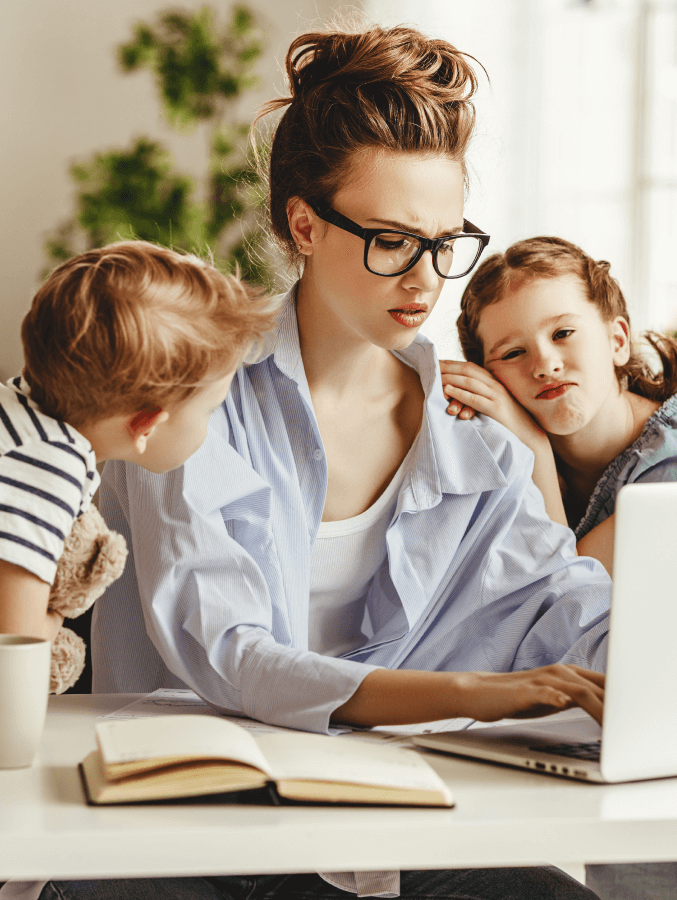 A woman is sitting at a table using a laptop computer while two children look on.