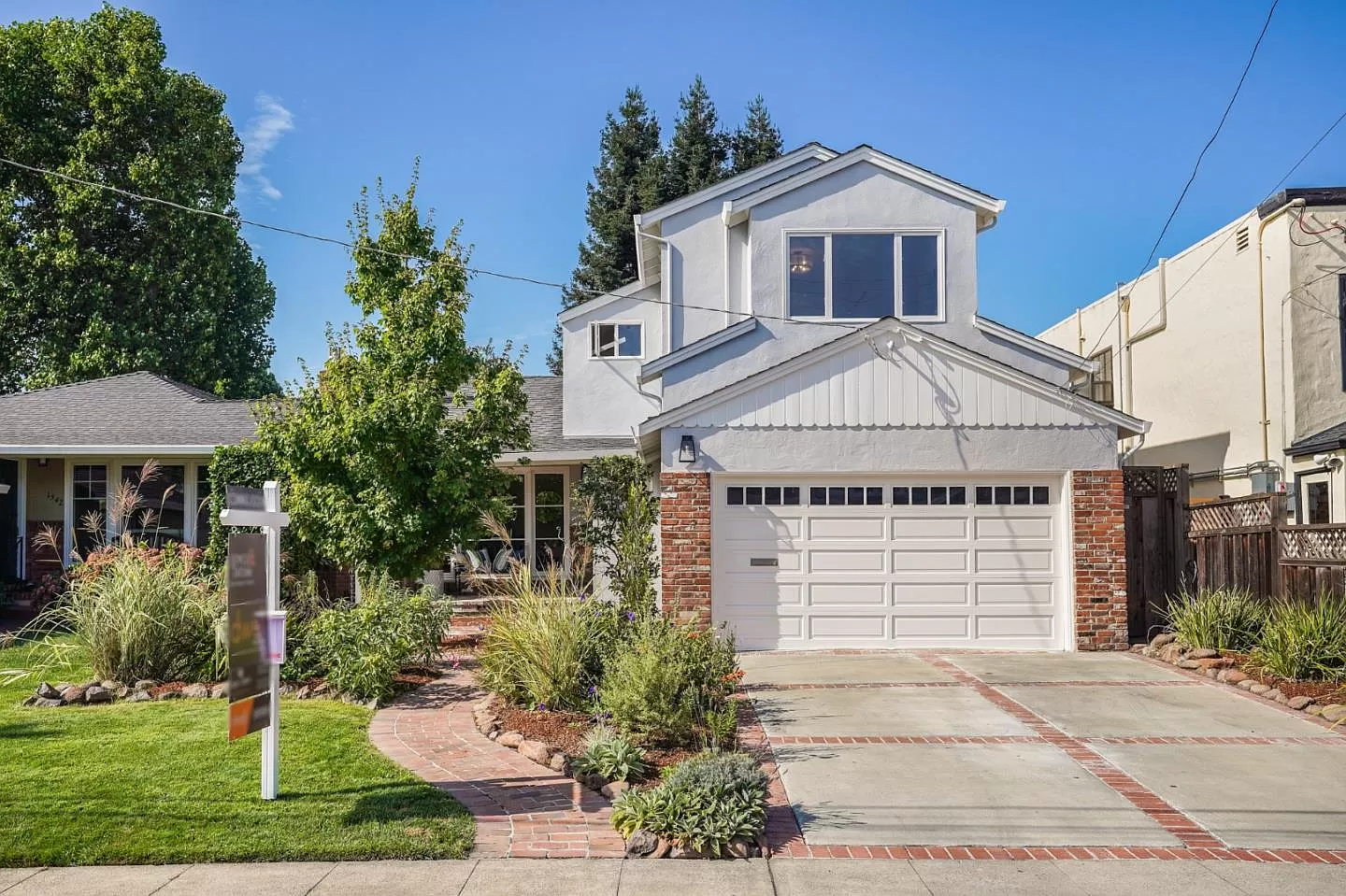 A white house with a garage and a for sale sign in front of it.