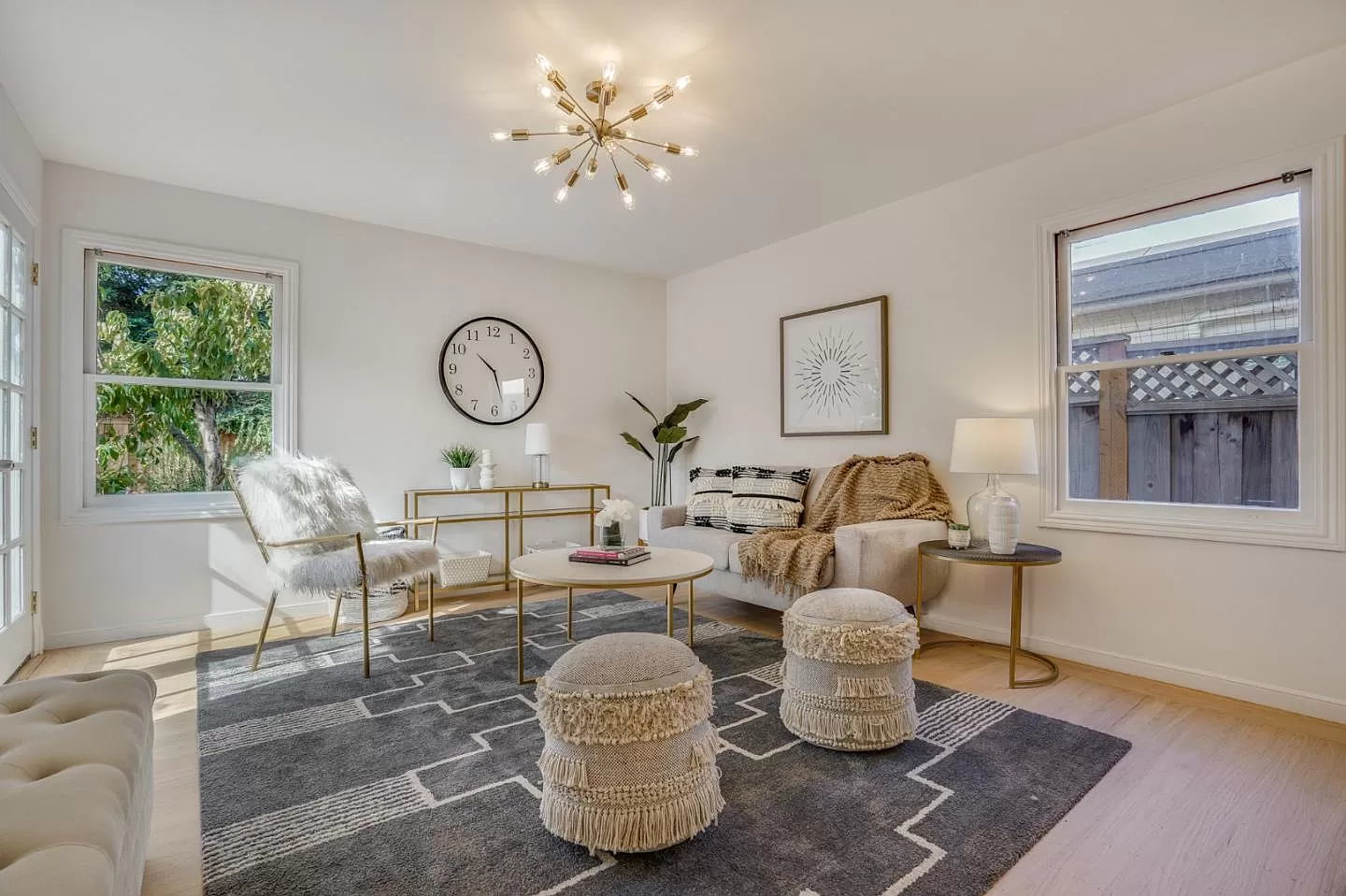 A living room with a couch , chairs , ottomans and a clock on the wall.