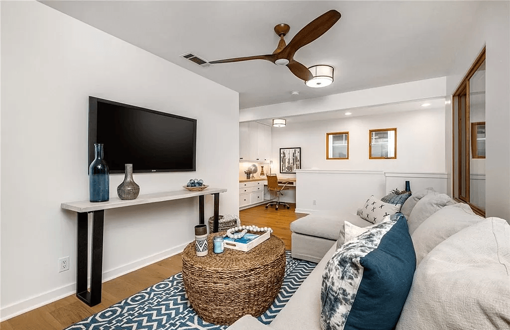 A living room with a couch , coffee table , television and ceiling fan.
