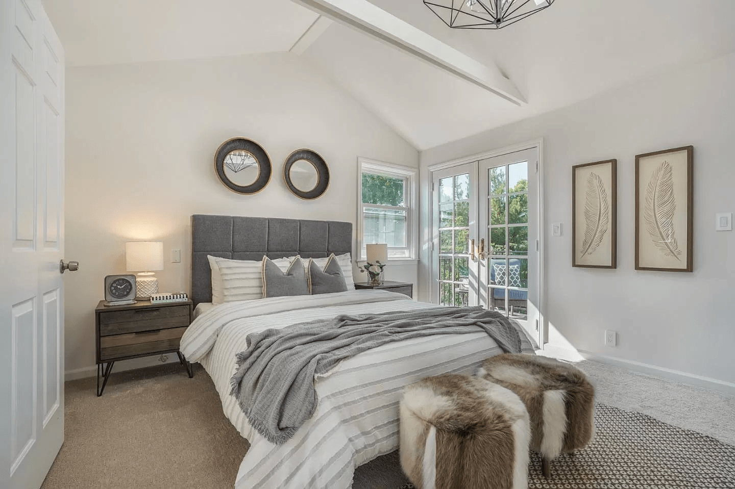 A bedroom with a king size bed , two ottomans , a nightstand , and a window.