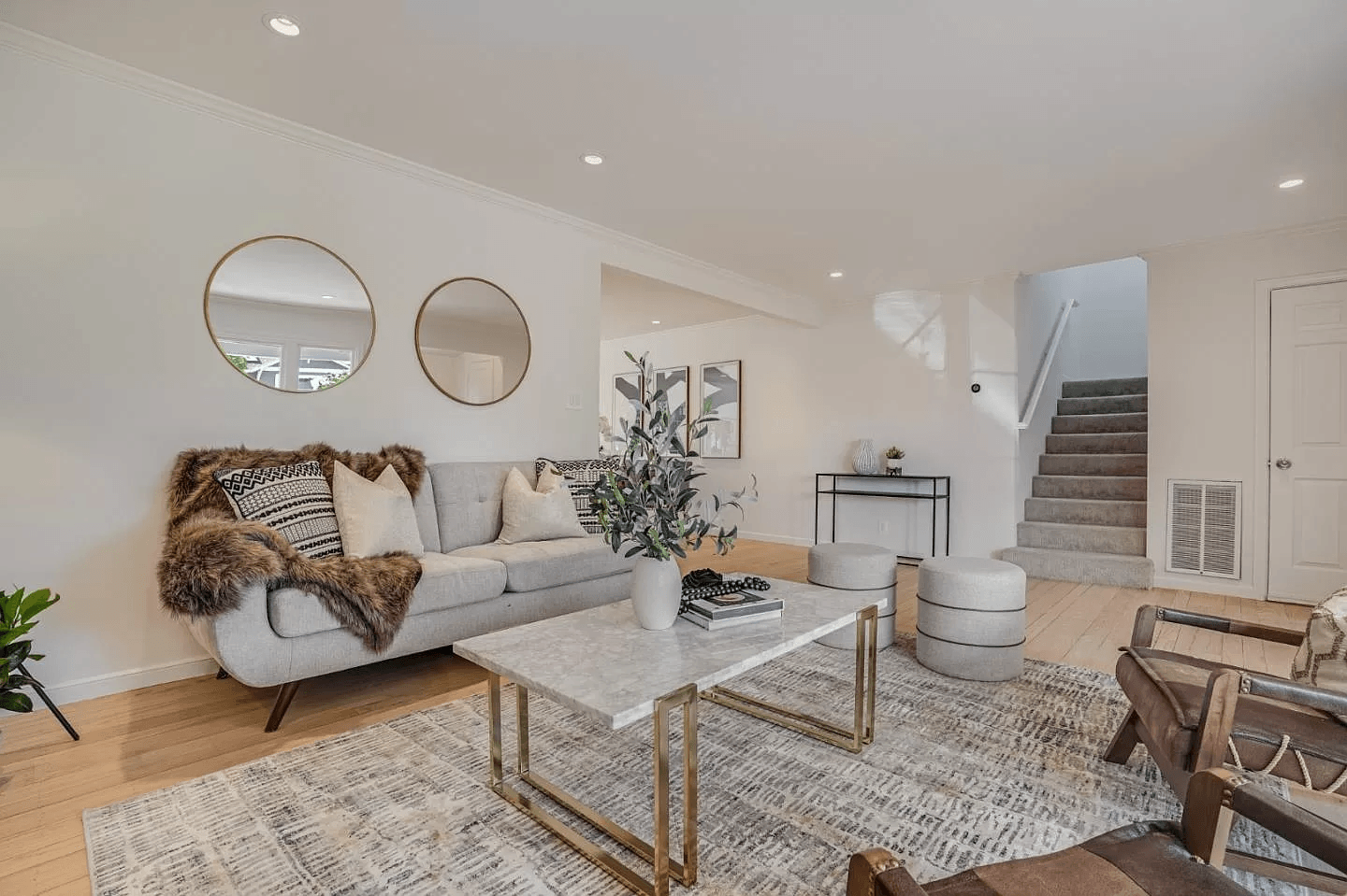A living room with a couch , coffee table , chairs and mirrors.