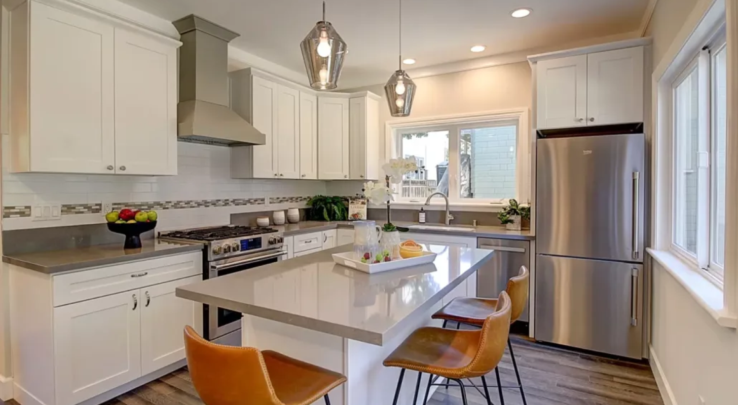 A kitchen with white cabinets , stainless steel appliances , and a large island.