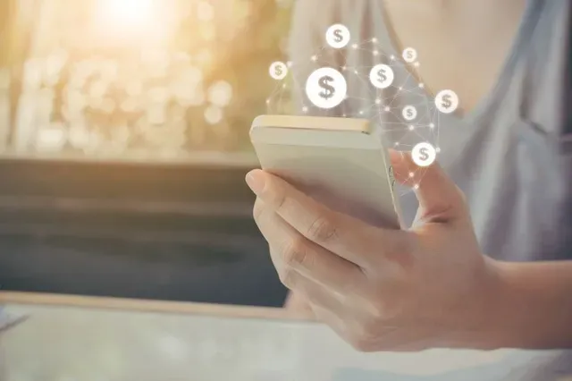 A woman is holding a cell phone with a dollar sign coming out of it.