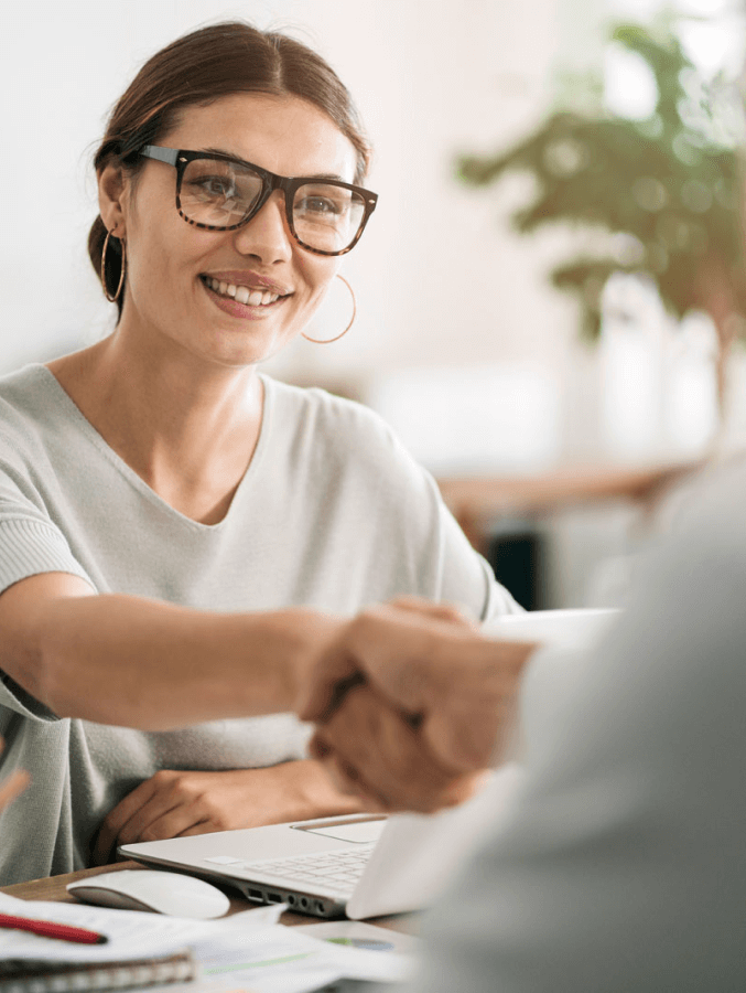 A woman wearing glasses is shaking hands with a man at a table.