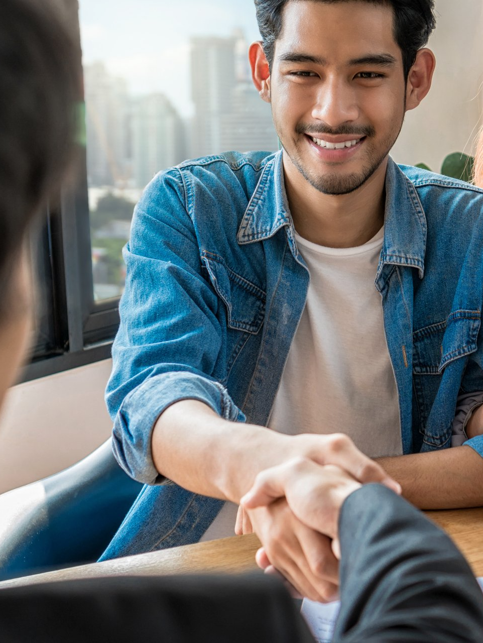 A man in a denim shirt is shaking hands with another man.