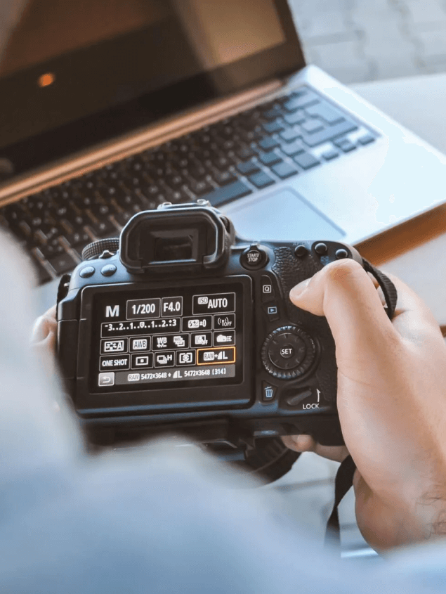 A person is holding a camera in front of a laptop.