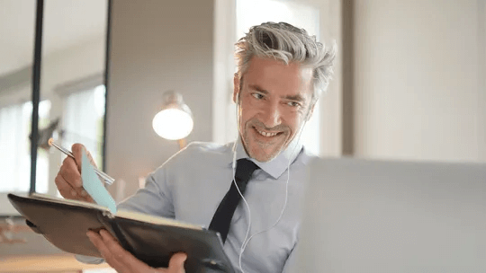 A man is sitting in front of a laptop computer holding a book and a tablet.