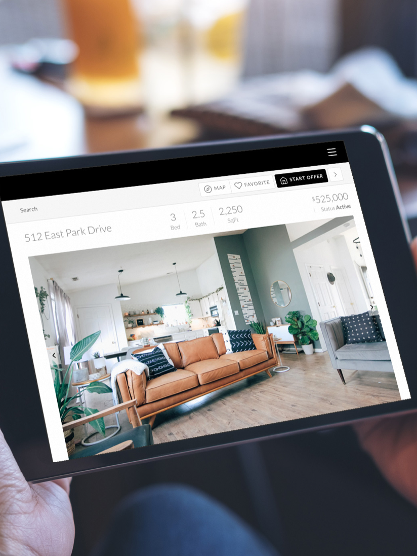 A person is holding a tablet with a picture of a living room on it.