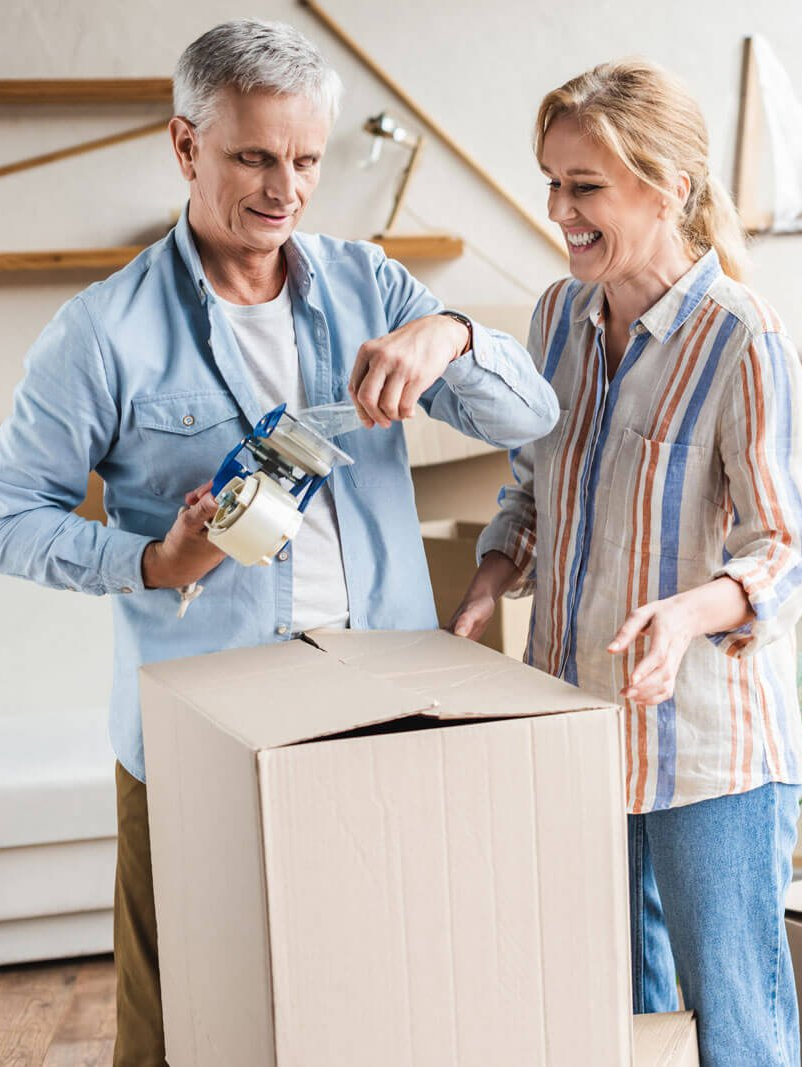 A man and a woman are taping a cardboard box together.