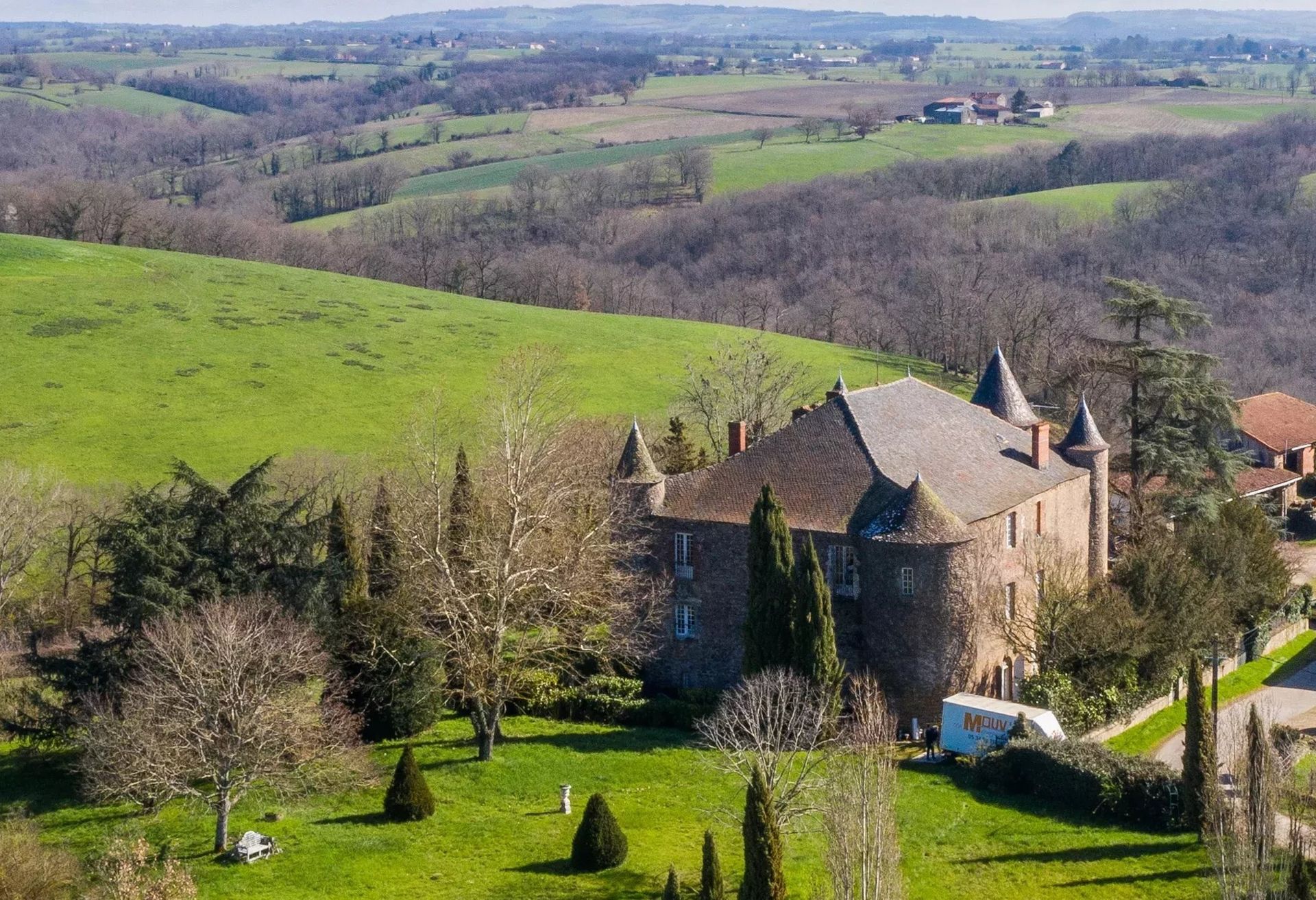 Un château de pierre aux multiples tourelles se dresse au milieu d'un paysage vallonné et verdoyant