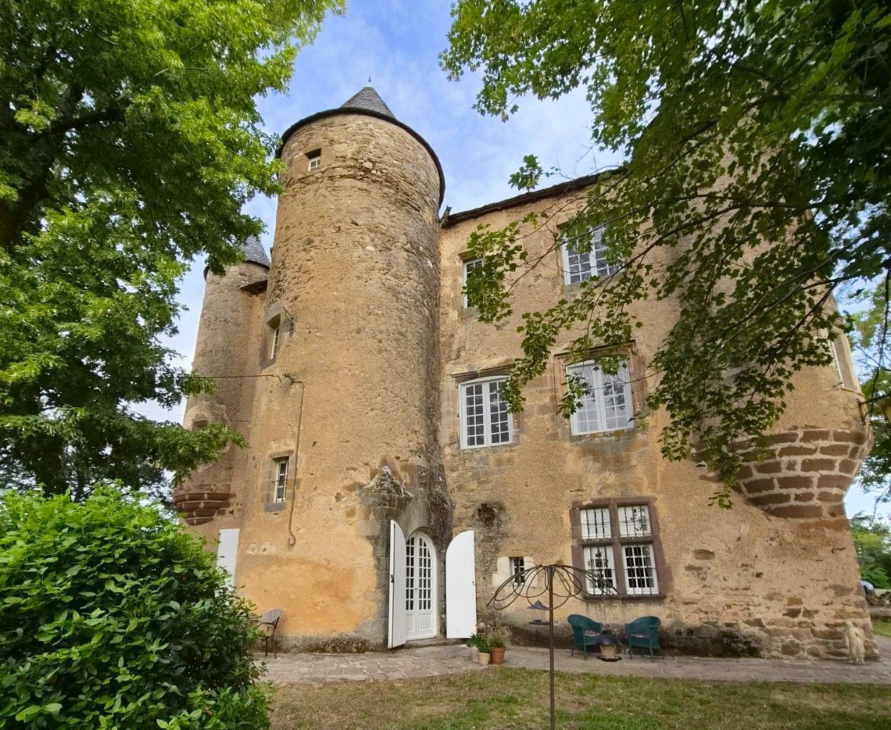 Stone castle with two turrets, multiple windows, set on a green lawn with trees in the background. historic-castle -tarn-france.jpg