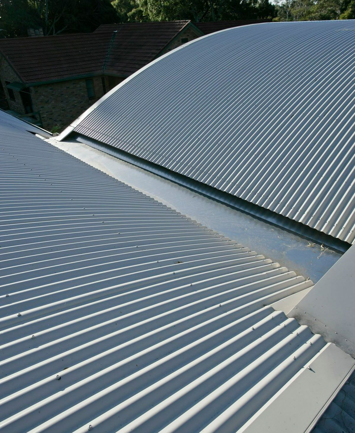 Silver corrugated metal roofs of two buildings; a shallow valley between them.