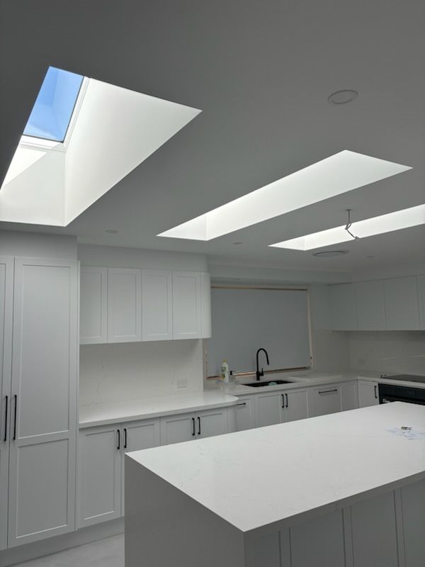 White kitchen with skylights, cabinets, and an island. Black faucet and hardware.