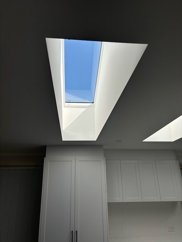 Skylight in a white ceiling, looking up to a blue sky. White cabinets below.
