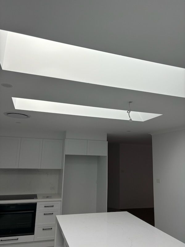 Modern white kitchen with recessed ceiling lights and a long, white island.