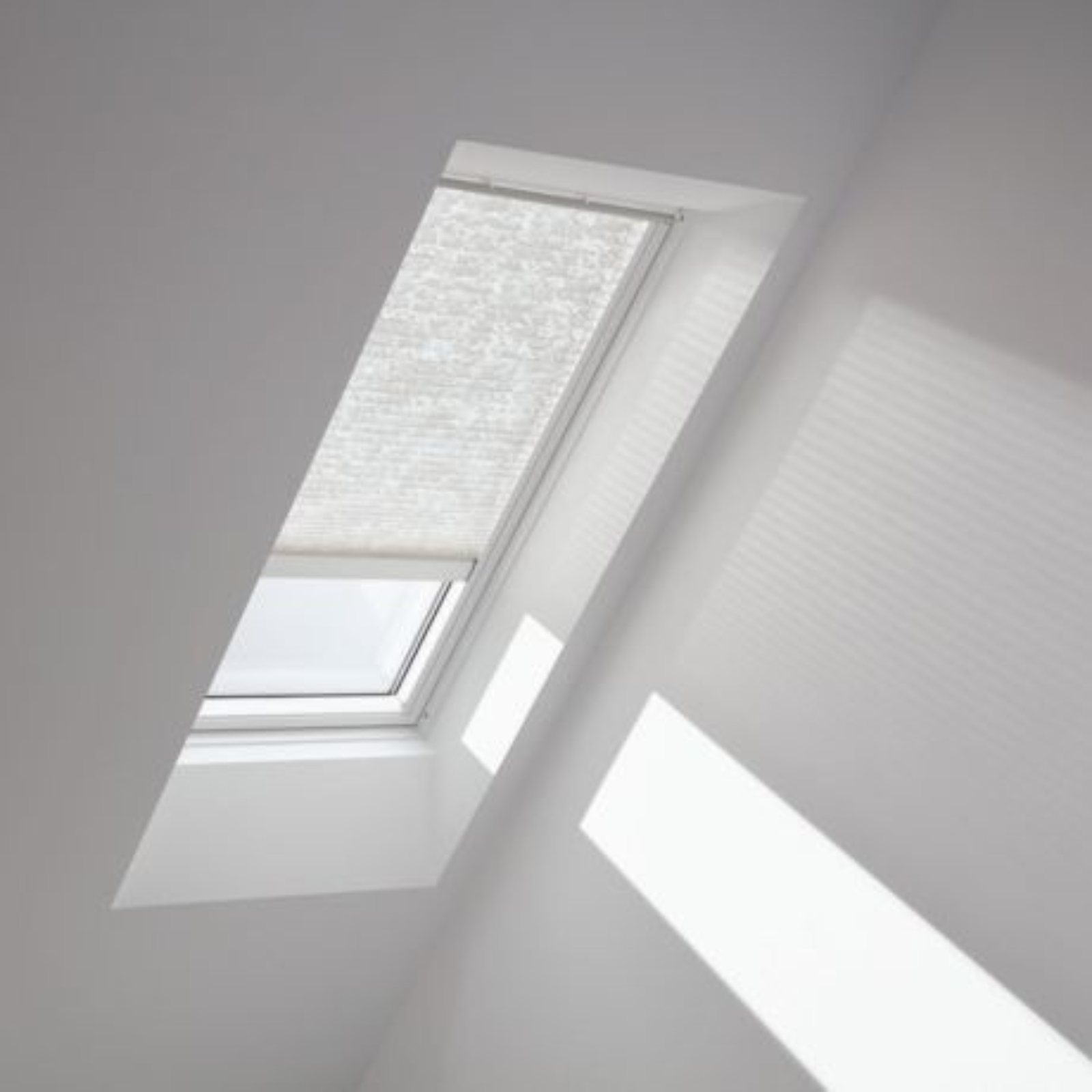 Skylight in a white room with sunlight streaming through. Window has a white, pleated shade.