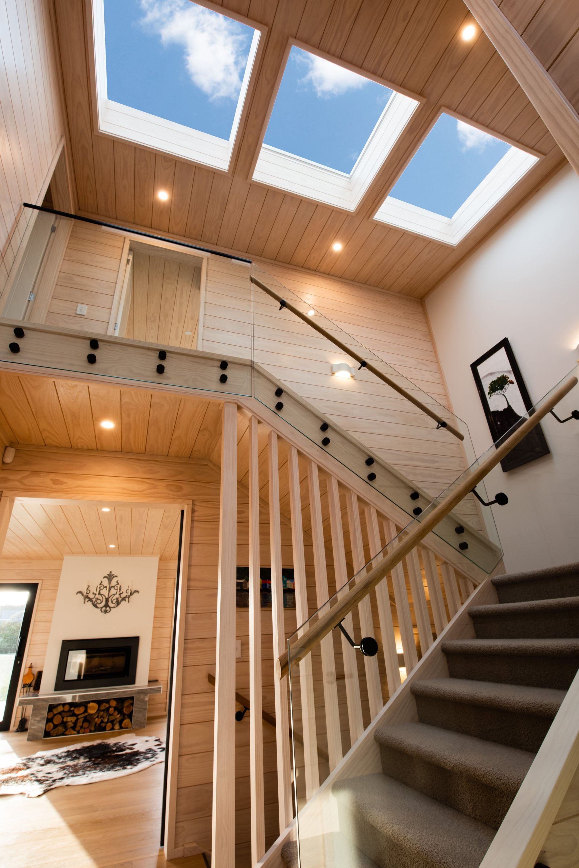 Interior view of a wooden staircase leading up to a loft with skylights. A fireplace is visible in the background.