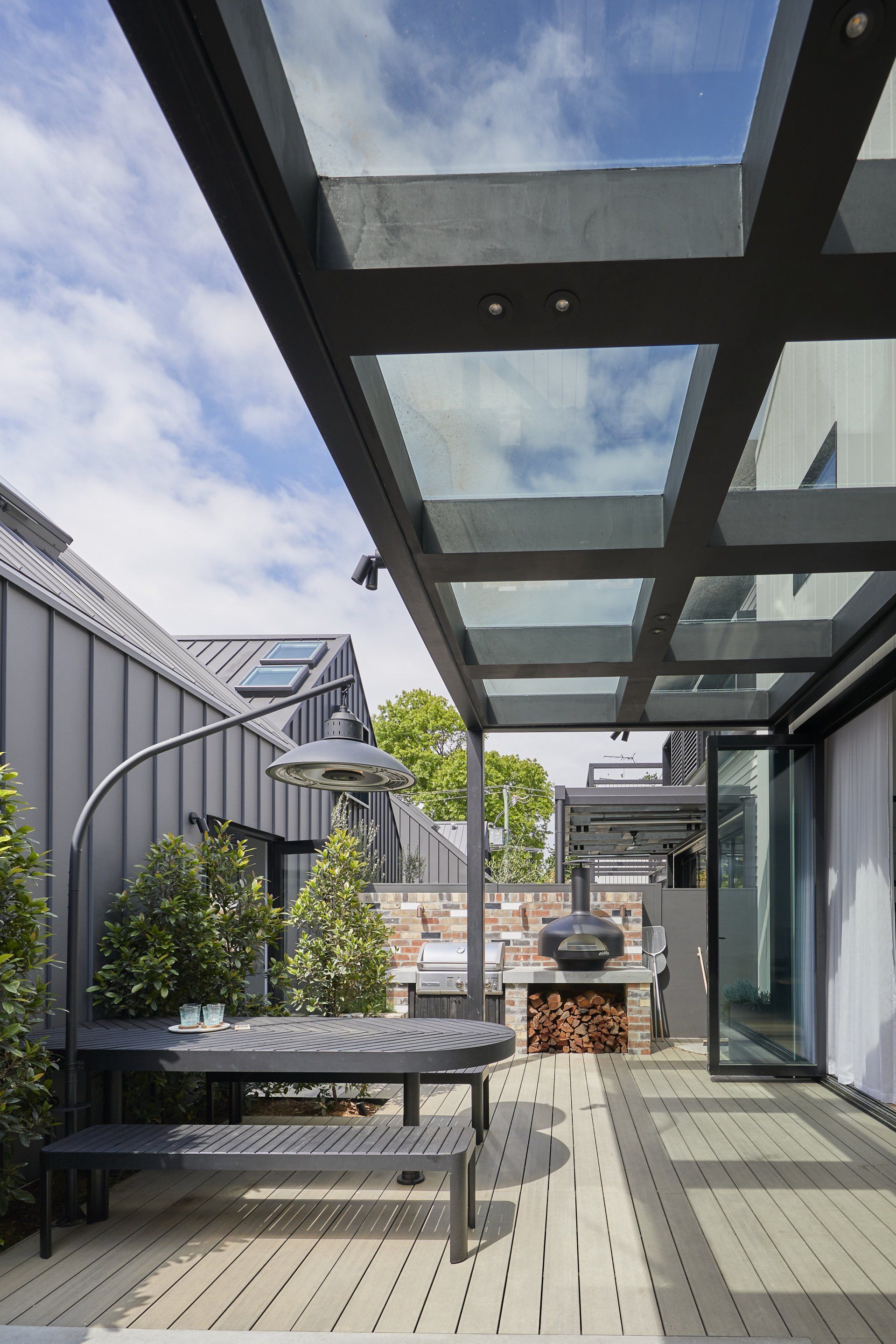 Outdoor patio with glass roof, grill, table, and benches. Modern architecture in gray tones.