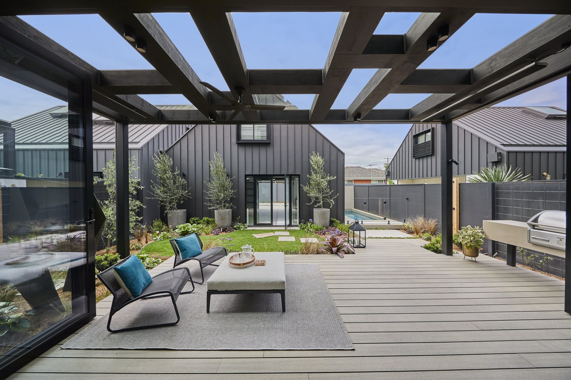 Patio with modern furniture, pergola, and black home in background.