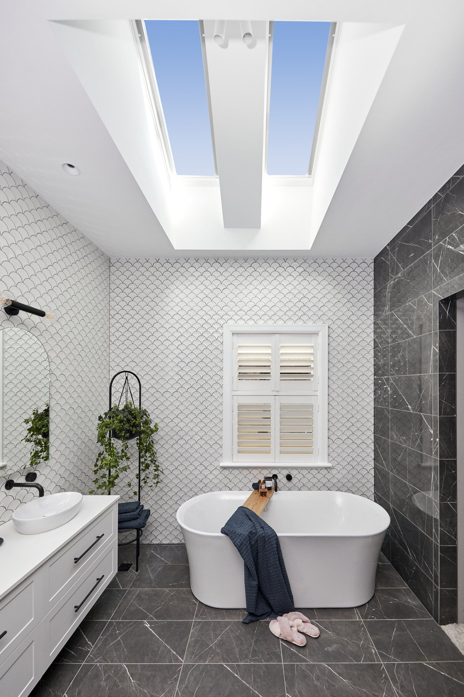 Modern bathroom with skylights, white tub, patterned walls, and a window.