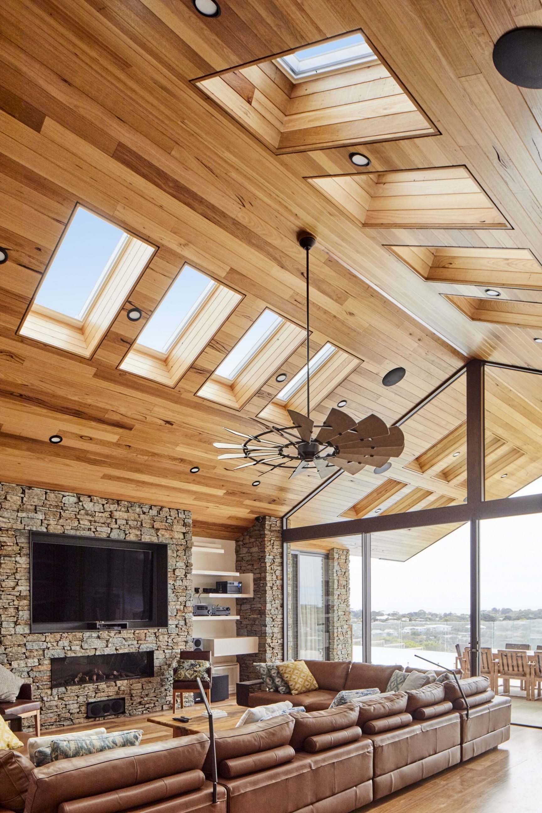 Living room with wooden ceiling, skylights, and leather sectional. Fireplace and window with view.