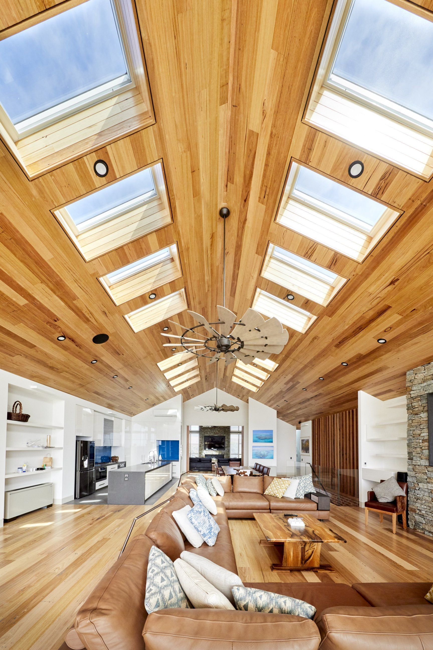 Spacious living room with wood ceiling and skylights, brown leather sofa, and wooden flooring.