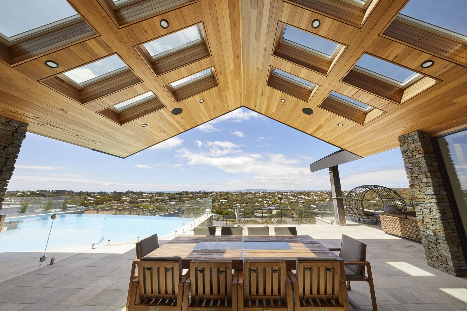 Patio with wooden ceiling and skylights, overlooking a pool and cityscape.