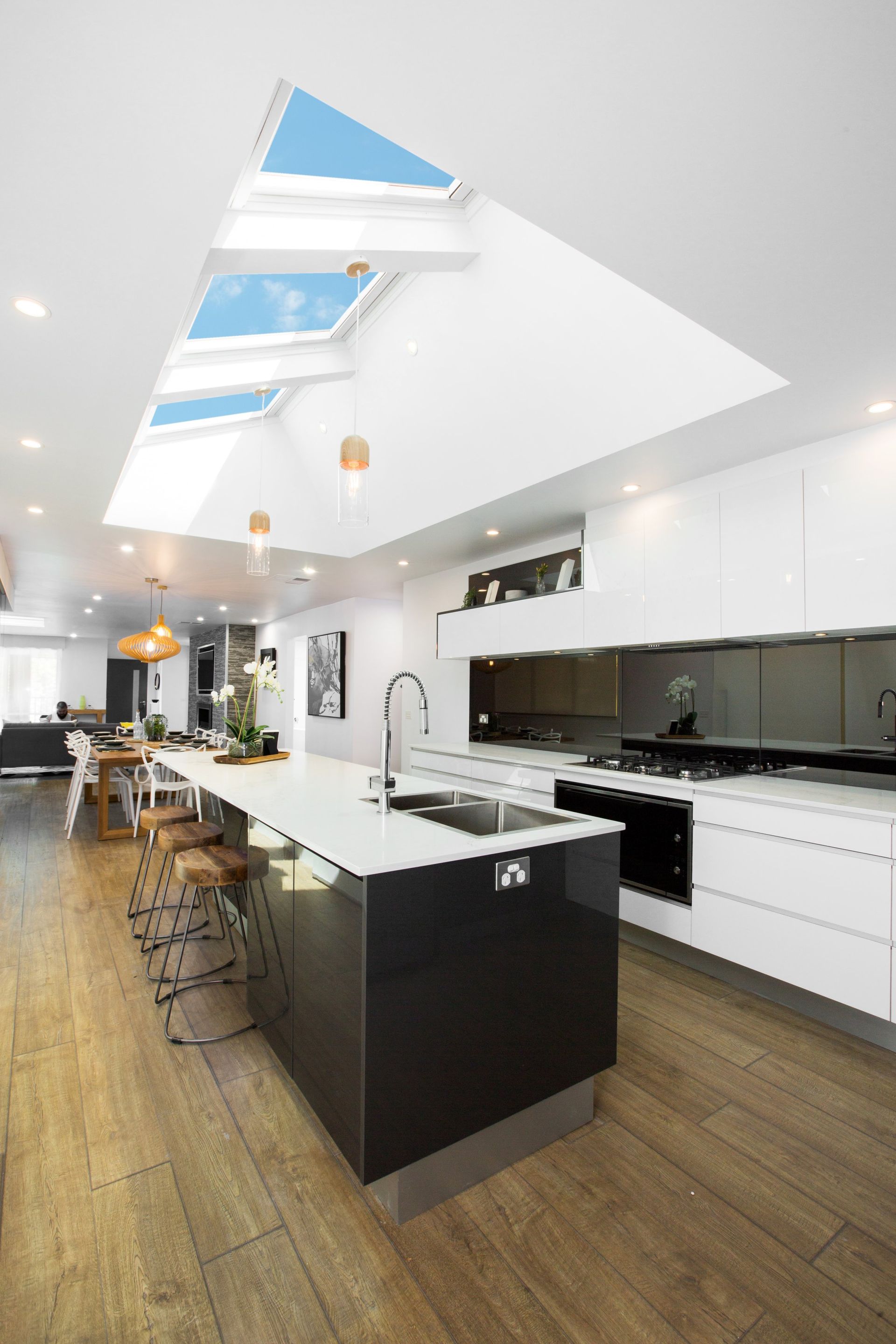 Modern kitchen with large skylights, island, white cabinets, and wooden floor.