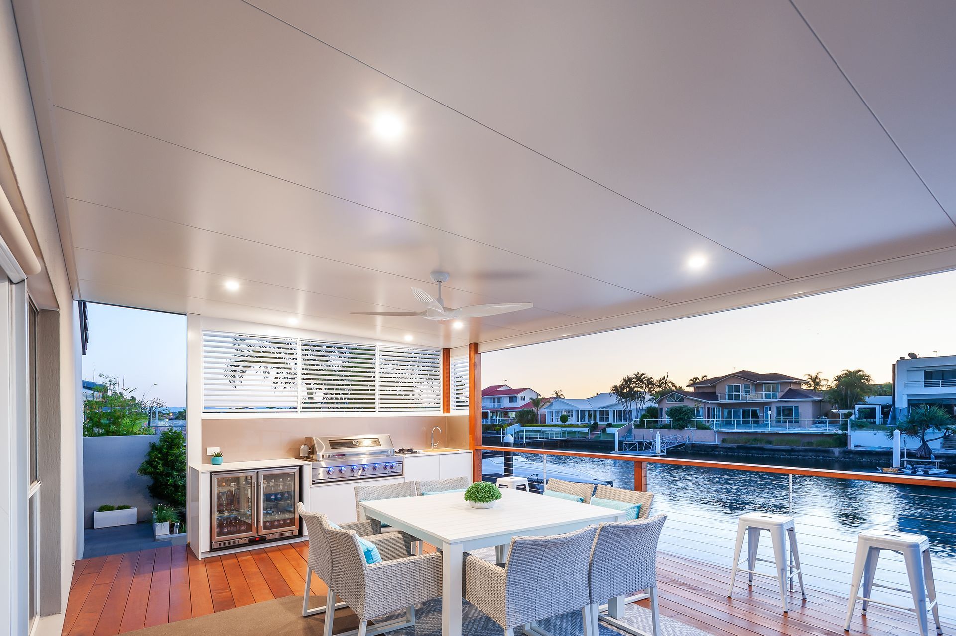 Patio with outdoor kitchen, waterfront view, dining table, and seating under a white ceiling.