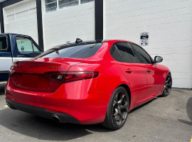 A red car is parked in front of a garage | In Stock Auto Outlet and Collision
