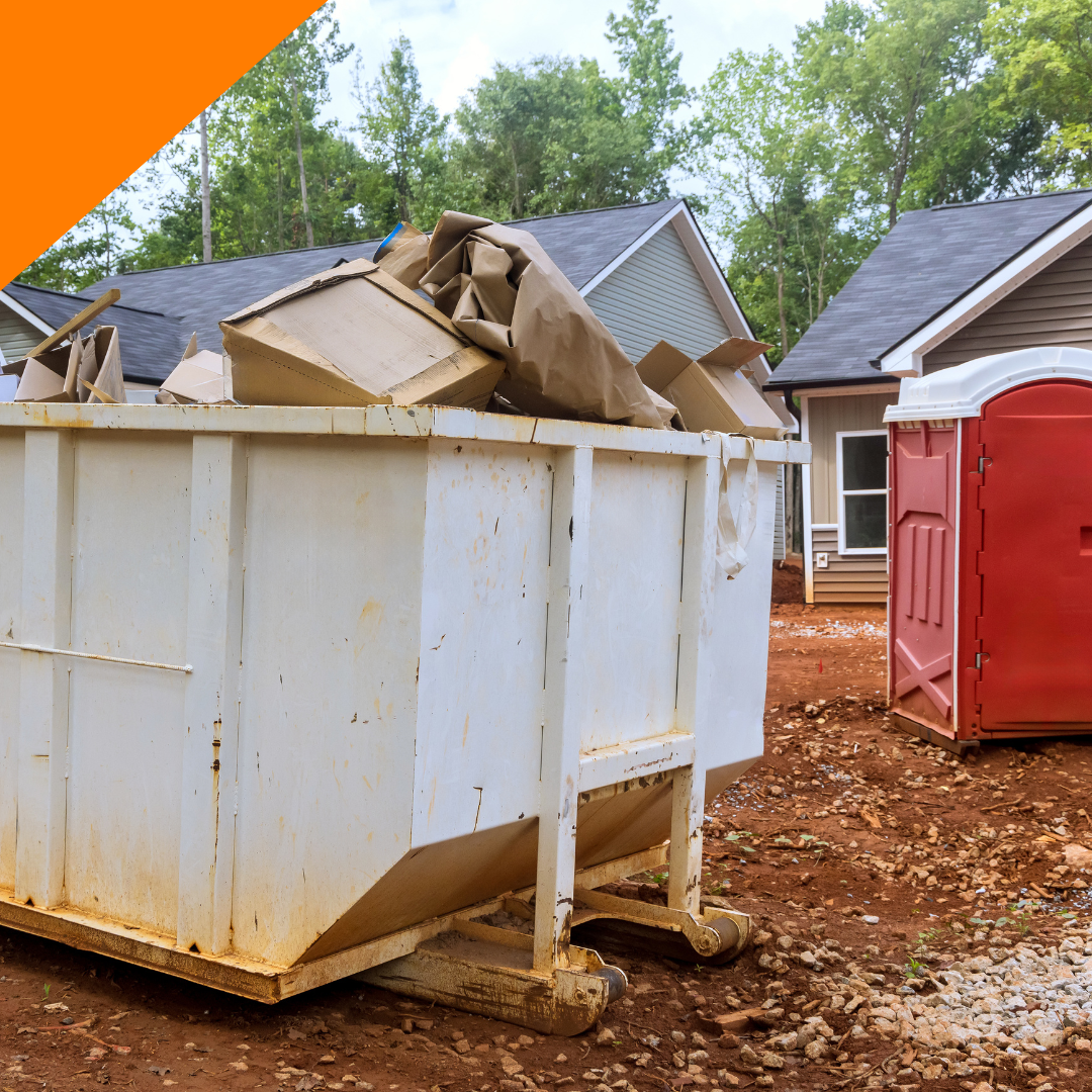 A white dumpster filled with cardboard boxes next to a red portable toilet.