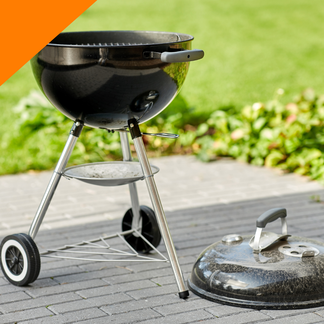 A black charcoal grill is sitting on a brick sidewalk